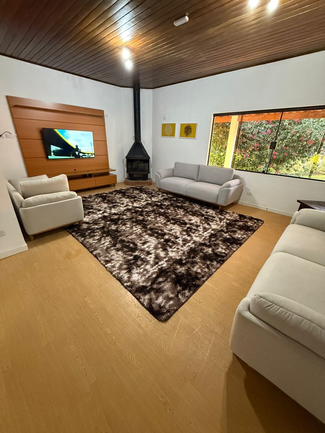 Sala de estar feminina com sofás claros, lareira, tapete e janelas para o jardim