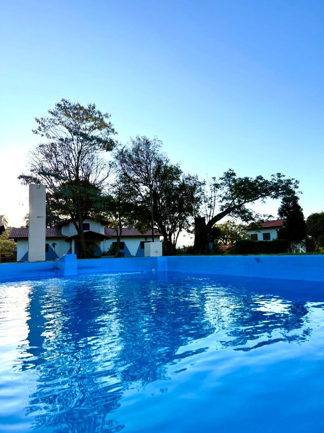 Piscina de água azul cercada por gramado e árvores na unidade feminina